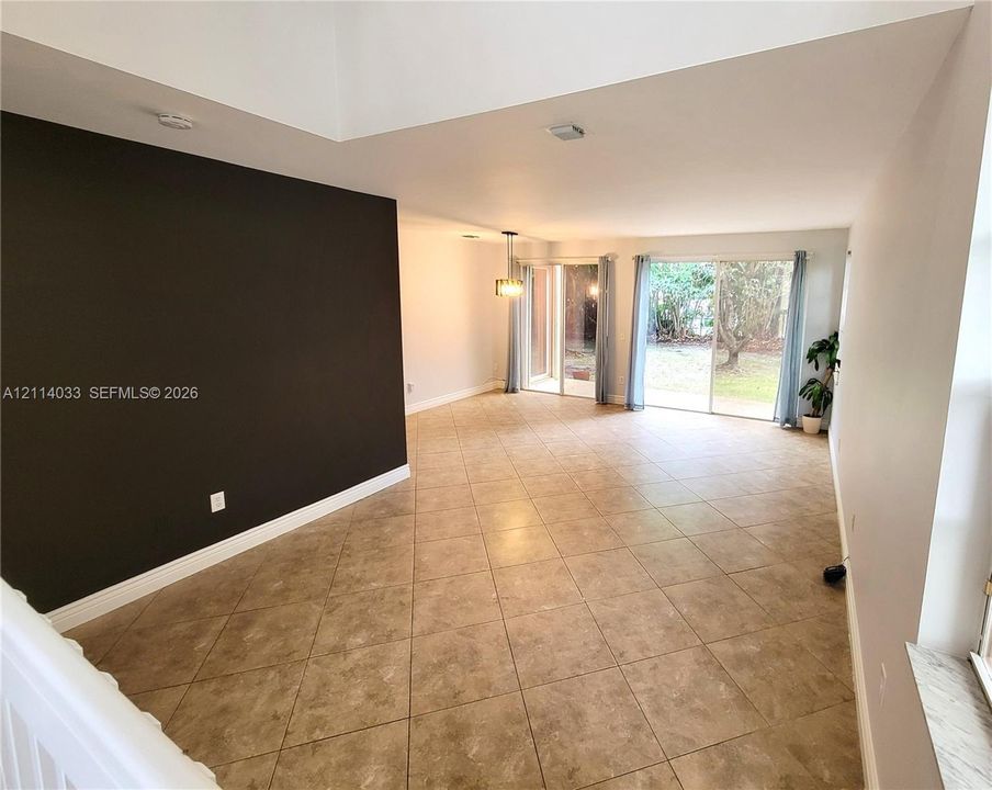 Spacious room featuring a vaulted ceiling, large-format tile flooring, a prominent accent wall, and dual sliding glass doors