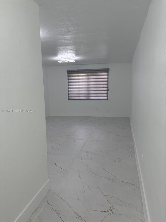 Neutral-toned, large-format tile flooring with veining pattern, flush-mount ceiling lighting, and horizontal window shade