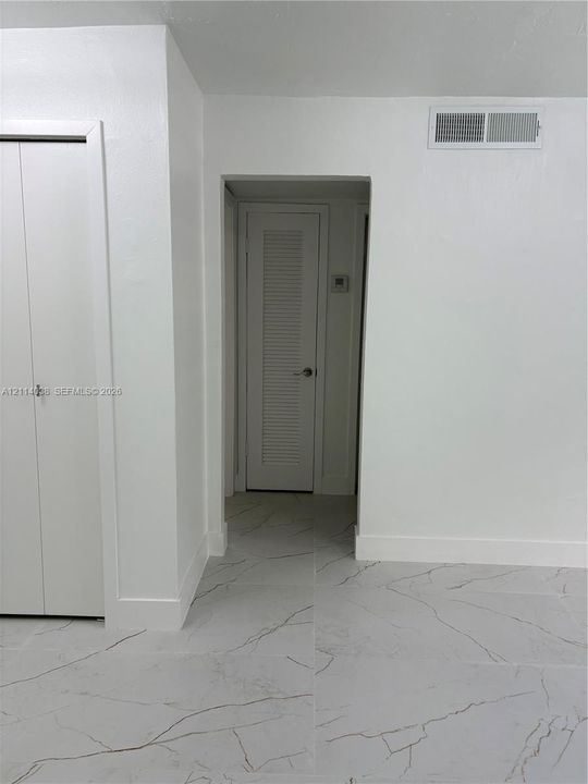 Large-format white tile flooring with grey veining, crisp white walls, and white louvered-panel closet doors