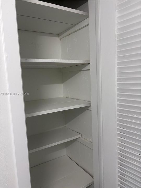 Built-in storage closet featuring five white-painted wooden shelves and louvered folding doors