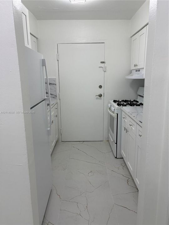 Kitchen featuring white shaker-style cabinetry, white countertops with veined detailing, large-format tile flooring, and integrated white appliances
