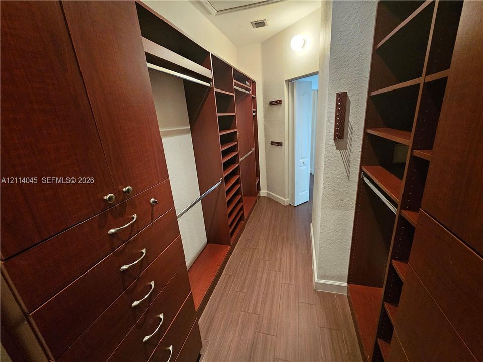 Custom walk-in closet featuring extensive dark wood-finish cabinetry, built-in shelving, integrated hanging rods, and wood-finish flooring