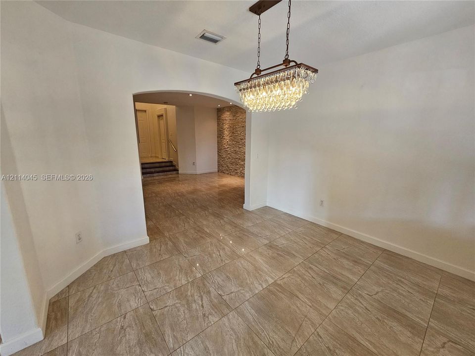 Large-format tile flooring, tiered crystal chandelier, arched entryway, and stone-accented wall finish