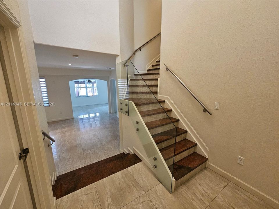 Staircase featuring dark stone treads, glass panel railings, and a metallic handrail, complemented by large-format tile flooring and high ceilings