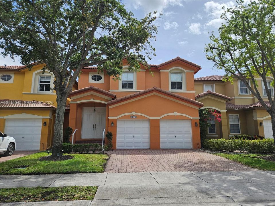 Two-story residence featuring a tile roof, stucco exterior, double-entry doors, and a paver driveway leading to a two-car garage
