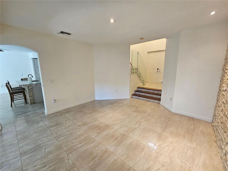 Large-format tile flooring, textured stone accent wall, glass panel staircase railing, recessed lighting, and double-door entry