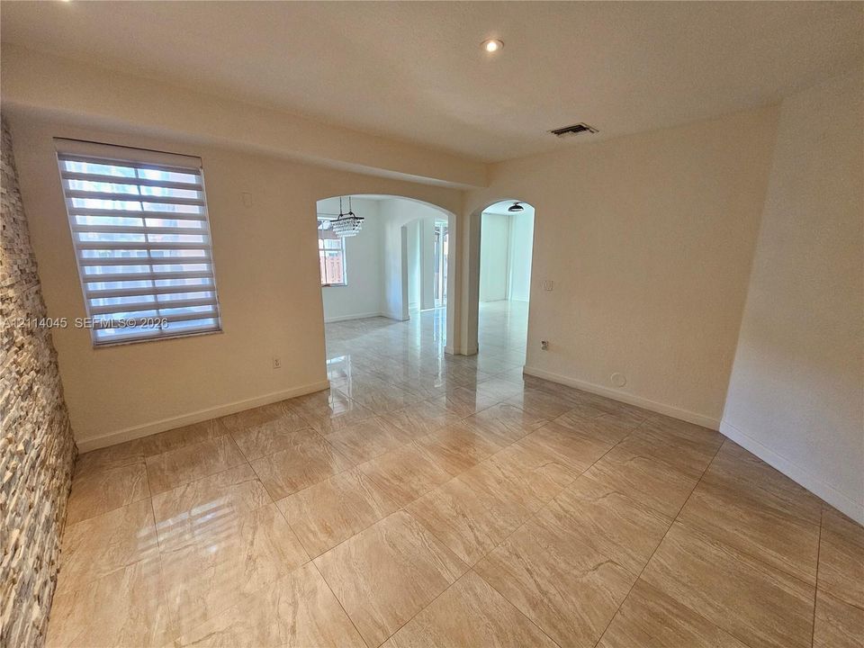 Interior space featuring large-format tile flooring, stacked stone wall accent, arched architectural openings, recessed lighting, and multi-layered window shades