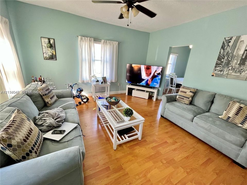 Living area featuring wood-finish flooring, central ceiling fan, and multi-pane windows with integrated blinds
