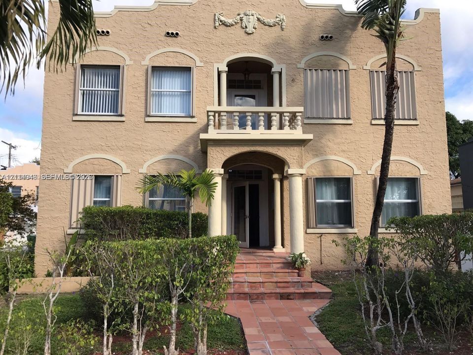 Mediterranean-style exterior featuring stucco masonry, arched window detailing, a second-story balcony with balustrade, and a terracotta tile walkway leading to a covered entryway with column supports