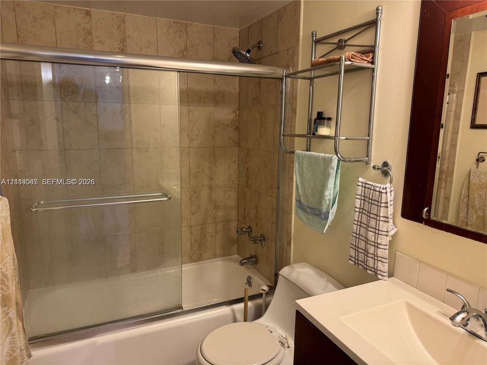 Bathtub and shower combination featuring a glass sliding enclosure and stone-finish tile surround, accompanied by a vanity with a white countertop and integrated sink