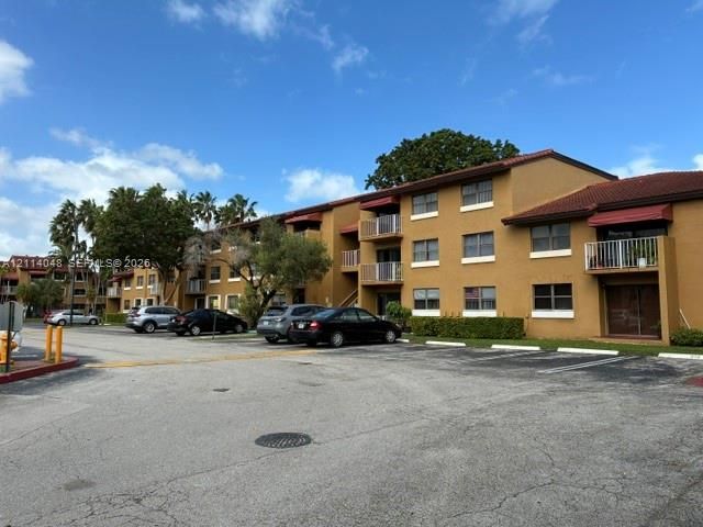 Three-story multi-unit structure with stucco exterior, tile roofing, metal balcony railings, and surface parking area