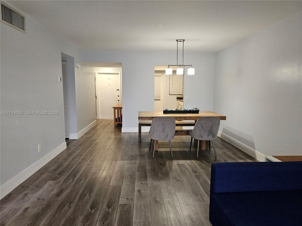 Open-concept interior featuring wood-finish flooring, neutral wall paint, and a modern three-light pendant fixture