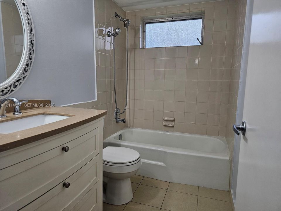 Bathroom featuring a vanity with a solid-surface countertop, an integrated sink, a built-in tub with a wall-mounted shower fixture, ceramic tile surround, and an inset window