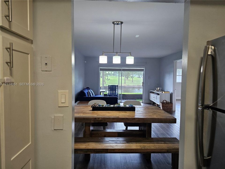Neutral-toned cabinetry with satin nickel pulls, wood-finish flooring, and a three-light linear pendant fixture, punctuated by sliding glass doors