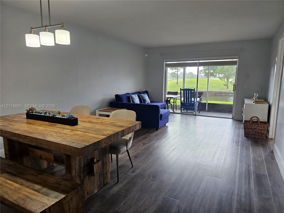 Open-concept interior featuring wood-finish flooring, a three-light linear pendant fixture, and sliding glass doors leading to a screened-in patio