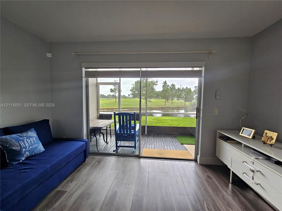 Interior featuring wood-finish flooring, sliding glass doors, and a screen-enclosed patio with interlocking patio tiles overlooking a pond