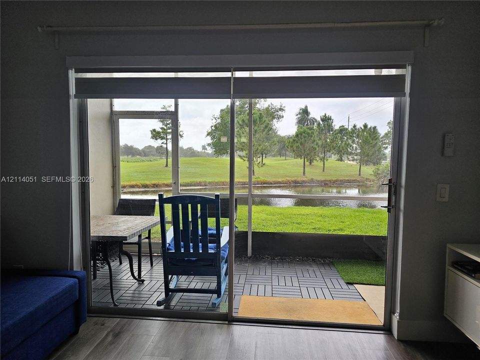 Sliding glass door opening to a screened-in patio featuring modular tile flooring, overlooking a pond and landscape