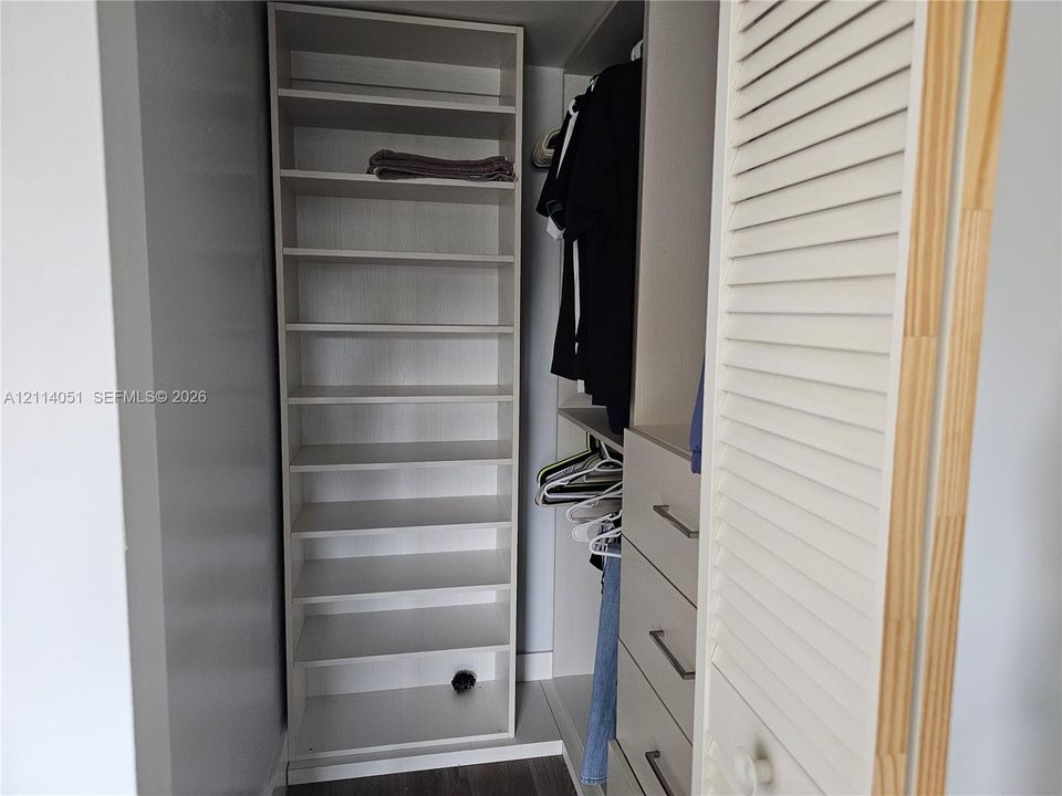 Custom closet organization system featuring vertical shelving, hanging rods, built-in drawers with horizontal bar pulls, and a louvered door