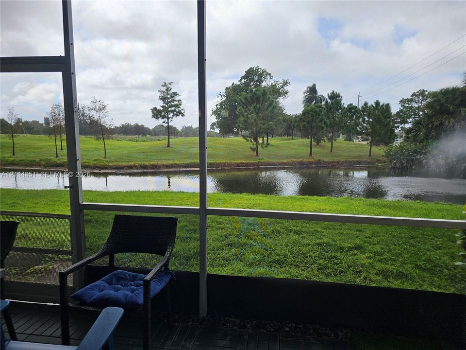 Screened-in patio featuring dark finished decking and a backdrop of a water feature, open green space, and mature trees