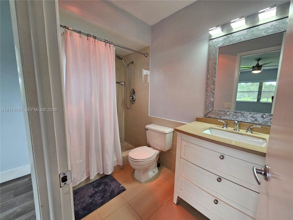 Bathroom featuring a white vanity with three drawers, a neutral-toned countertop with an integrated sink, a framed mirror, a three-bulb light fixture, and a tile-surround shower