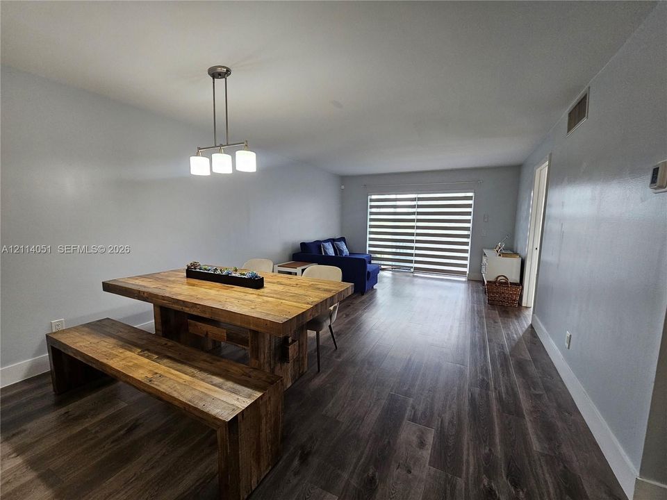 Open-concept interior featuring wood-finish flooring, a three-light pendant fixture, and sliding glass doors with horizontal blinds