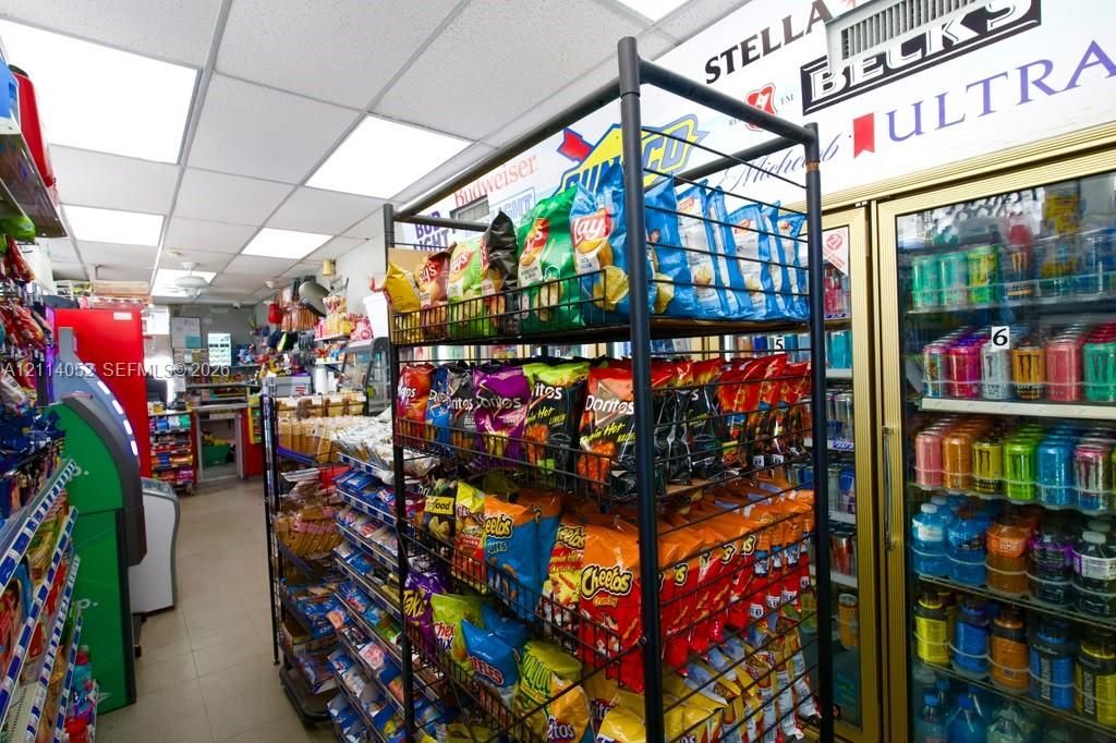 Commercial interior featuring a drop ceiling with recessed panel lighting, multi-tier metal display shelving, and glass-front refrigeration units