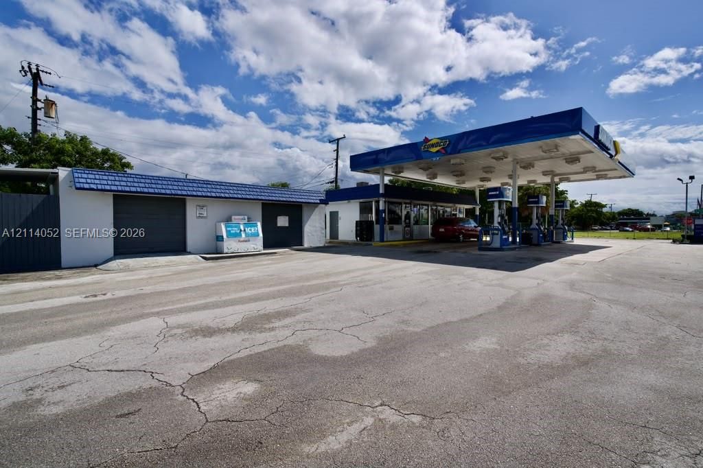 Commercial site featuring a paved asphalt lot, multi-bay fuel canopy, structural service building with roll-up doors, and integrated lighting fixtures