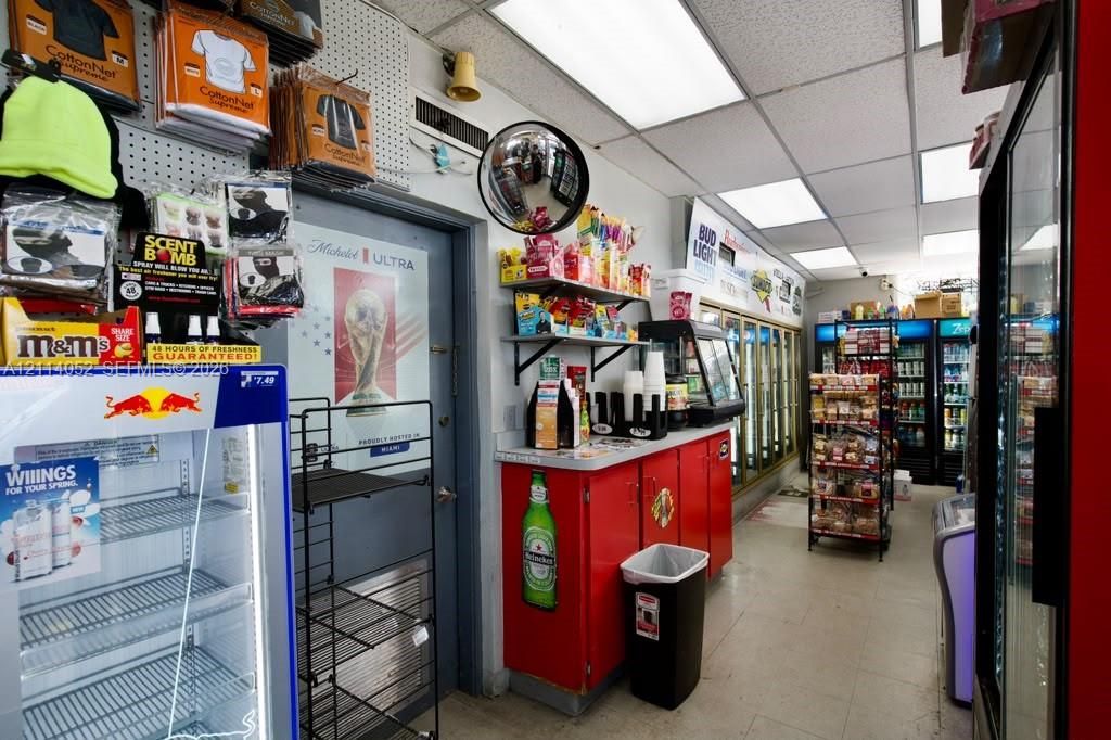 Commercial interior space featuring a drop ceiling with recessed lighting, multiple full-height glass-door refrigeration units, red cabinetry with solid surface countertops, and pegboard wall display systems