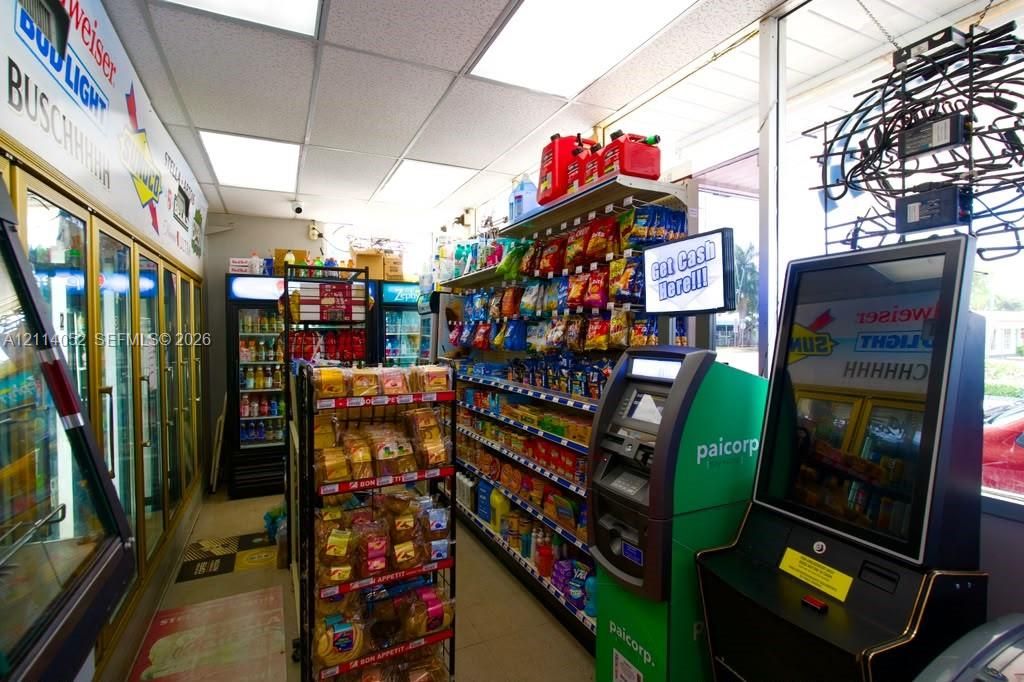 Commercial retail space featuring multi-door reach-in refrigeration units, expansive wall-mounted shelving, integrated ATM kiosk, and large-format glass storefront windows