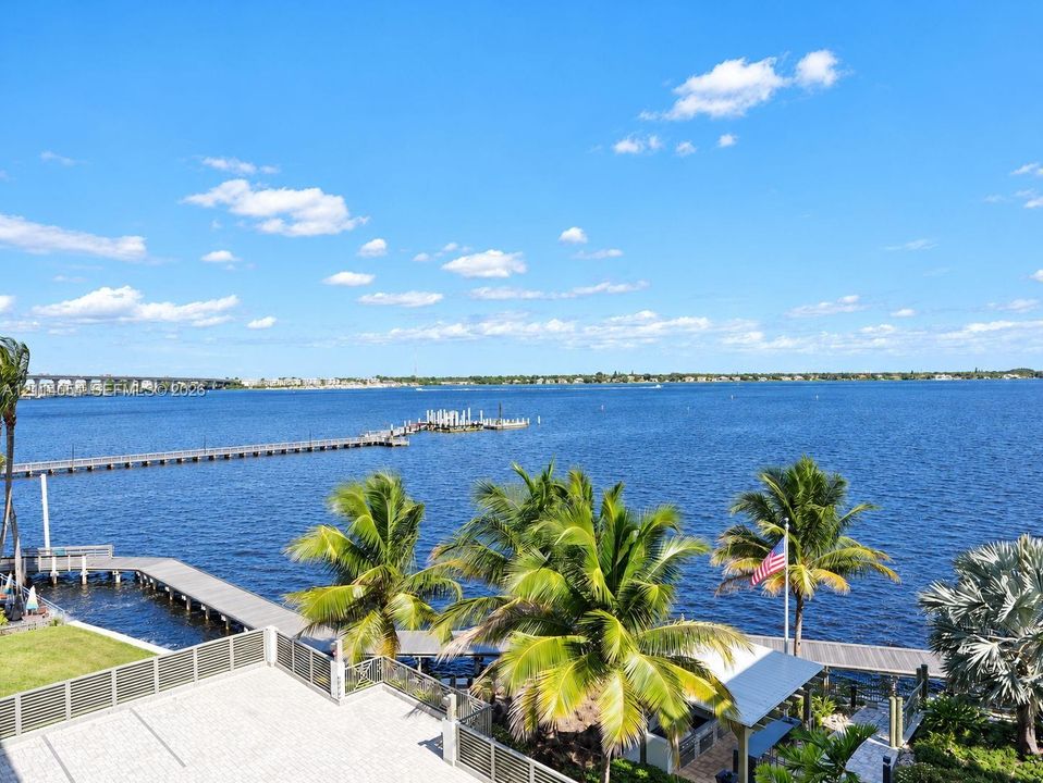 Waterfront terrace featuring stone paving, metal railings, mature palm trees, a dedicated boat dock, and direct access to open water