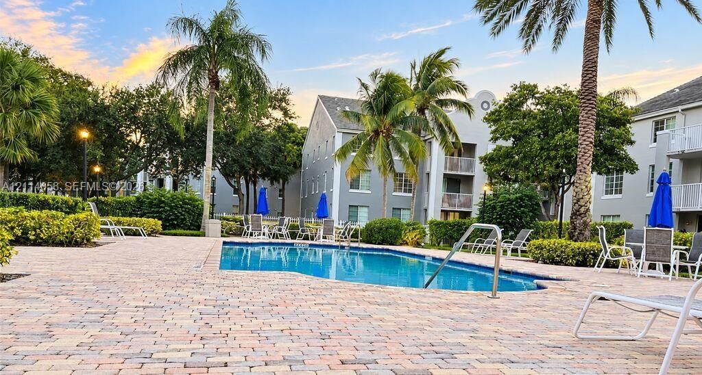 Swimming pool with paver decking, lush perimeter landscaping, and mature palm trees