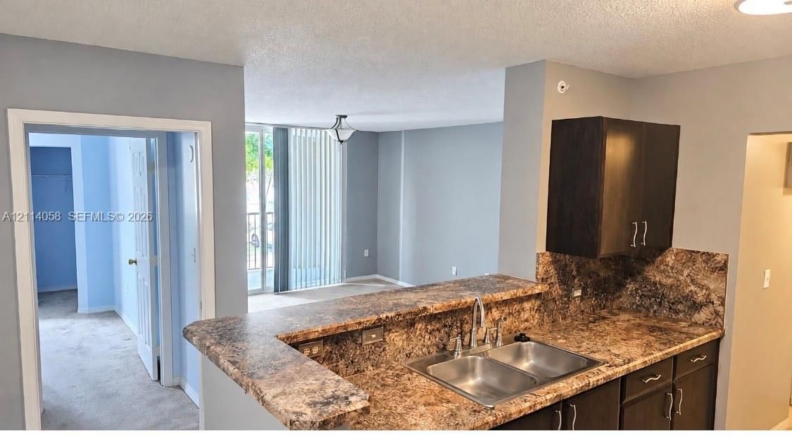 Kitchen featuring a breakfast bar, dark-toned cabinetry, dual-basin stainless steel sink with a high-arch faucet, and patterned stone-finish countertops