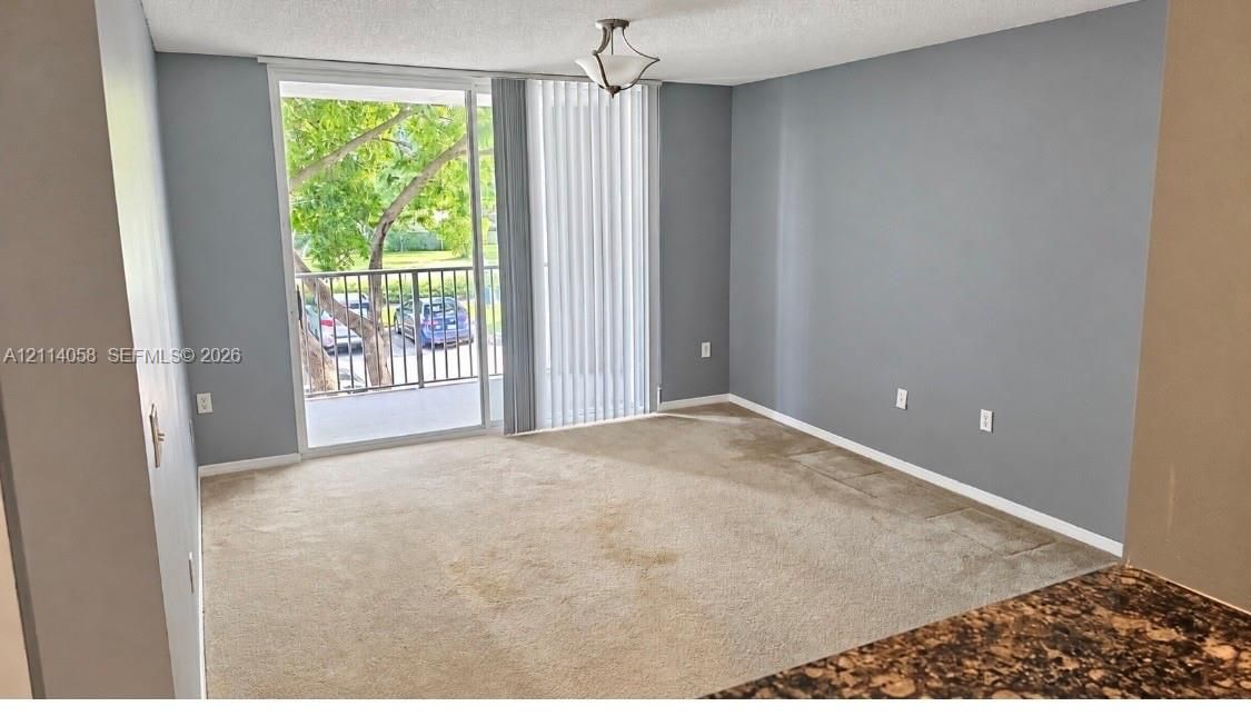 Living area featuring neutral-toned carpeting, sliding glass doors, a private balcony with metal railing, and a ceiling-mounted light fixture