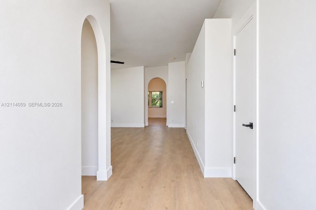 Interior space featuring arched doorways, wood-finish flooring, and minimalist white walls with matte black hardware