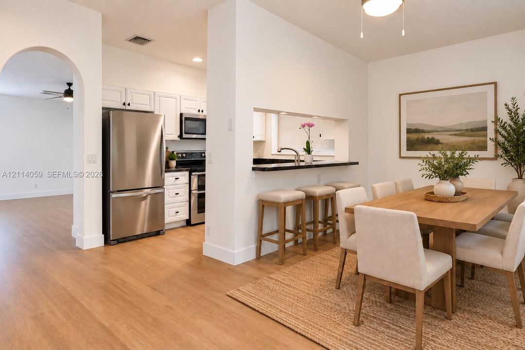 Kitchen featuring white cabinetry, stainless steel appliances, and a pass-through bar with a dark countertop, complemented by light wood-finish flooring and an arched entryway