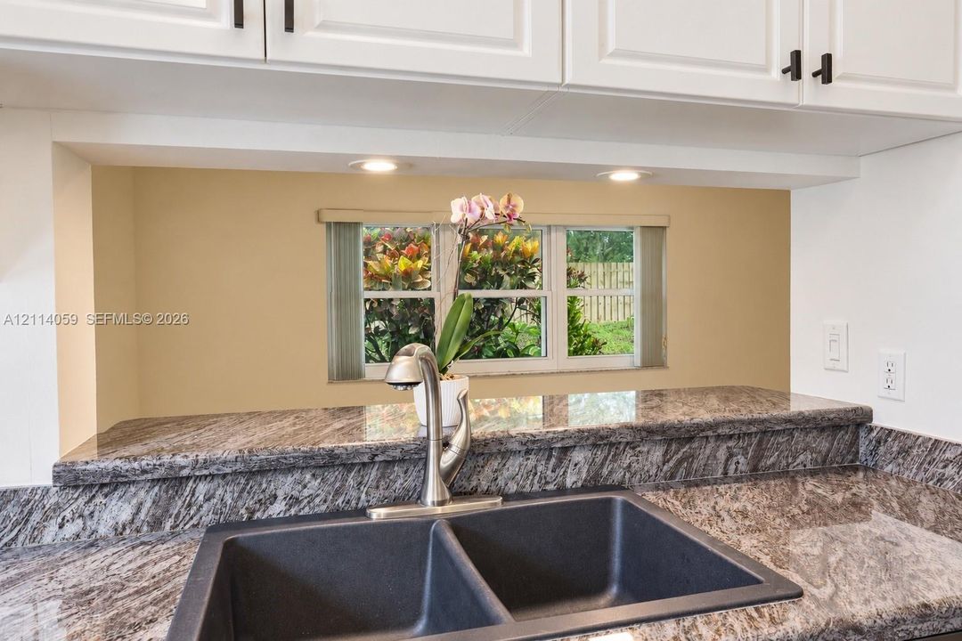 Kitchen featuring stone-finish countertops, undermount double-basin sink, high-arch faucet, white cabinetry with matte black hardware, and recessed lighting