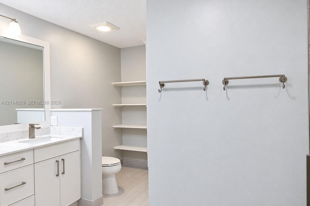 Bathroom featuring white cabinetry, stone-finish vanity countertop, undermount sink, built-in wall shelving, and dual brushed-nickel towel bars
