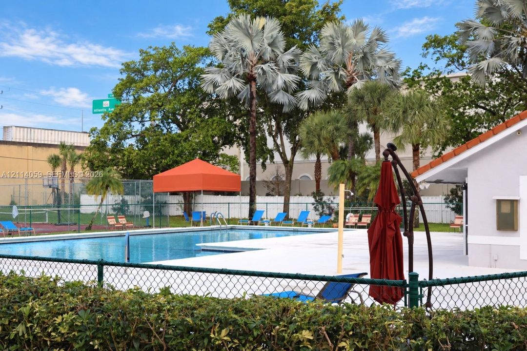 Swimming pool with concrete deck, chain-link perimeter fencing, and tennis court with backboard