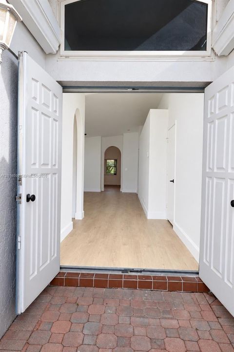 Double front entry doors with transom window, wood-finish flooring, and arched interior doorways