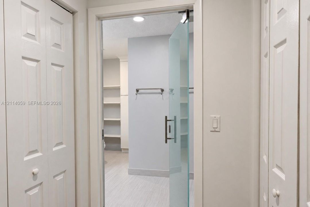 Frameless frosted glass door with a brushed metal handle, recessed ceiling lighting, built-in open shelving, and dual white paneled folding doors