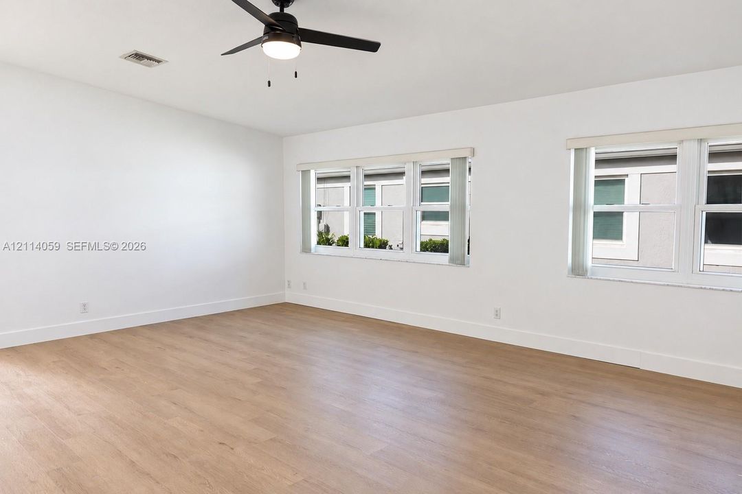 Neutral-toned interior space featuring wood-finish flooring, dual windows, and a matte black ceiling fan with integrated lighting