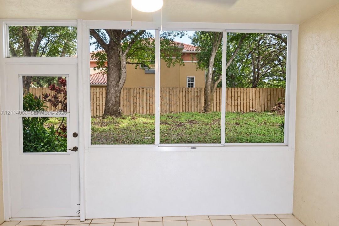 Enclosed sunroom featuring large pane windows, tile flooring, a ceiling-mounted light fixture, and an exterior door providing access to the fenced backyard