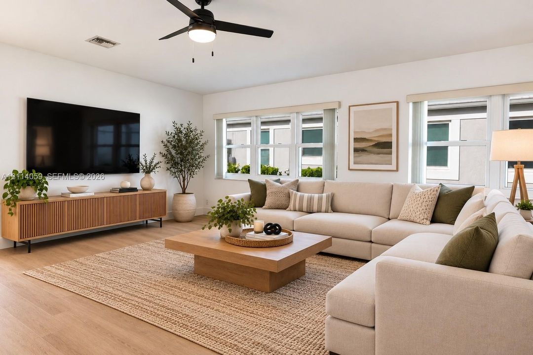 Living area featuring wood-finish flooring, matte black ceiling fan with integrated lighting, neutral wall palette, and expansive multi-pane window configuration