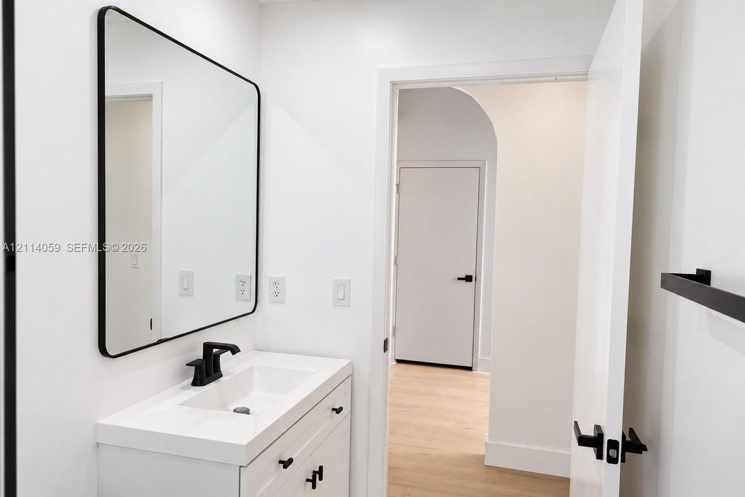 Modern white vanity with a rectangular sink, matte black faucet, rounded rectangular mirror, and matte black hardware featuring an arched doorway entry