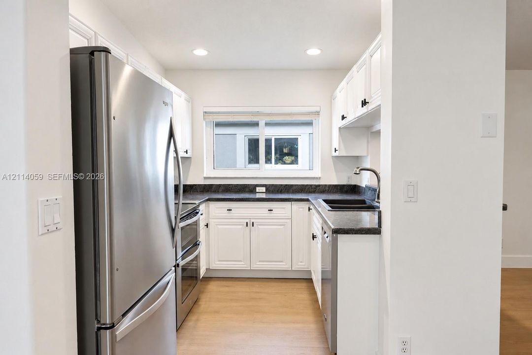 Kitchen featuring white shaker-style cabinetry, dark stone-finish countertops, stainless steel appliances, and wood-finish flooring