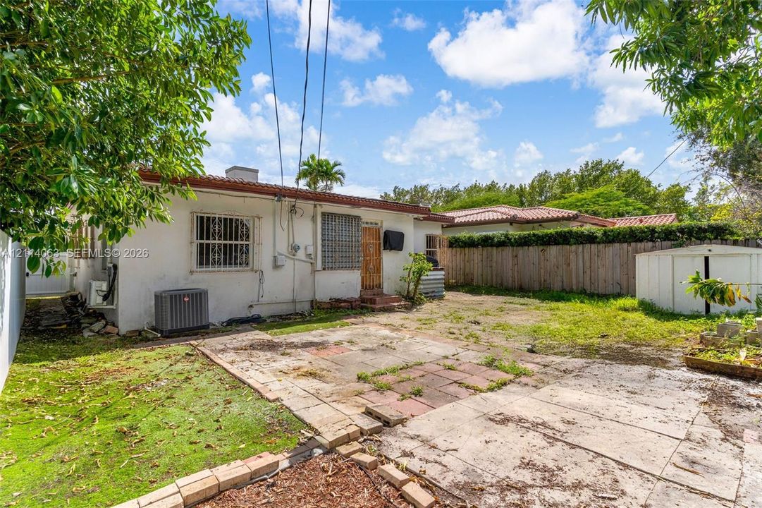 Rear exterior featuring a stucco facade, stone-paver patio area, wood-plank fencing, and a detached storage structure