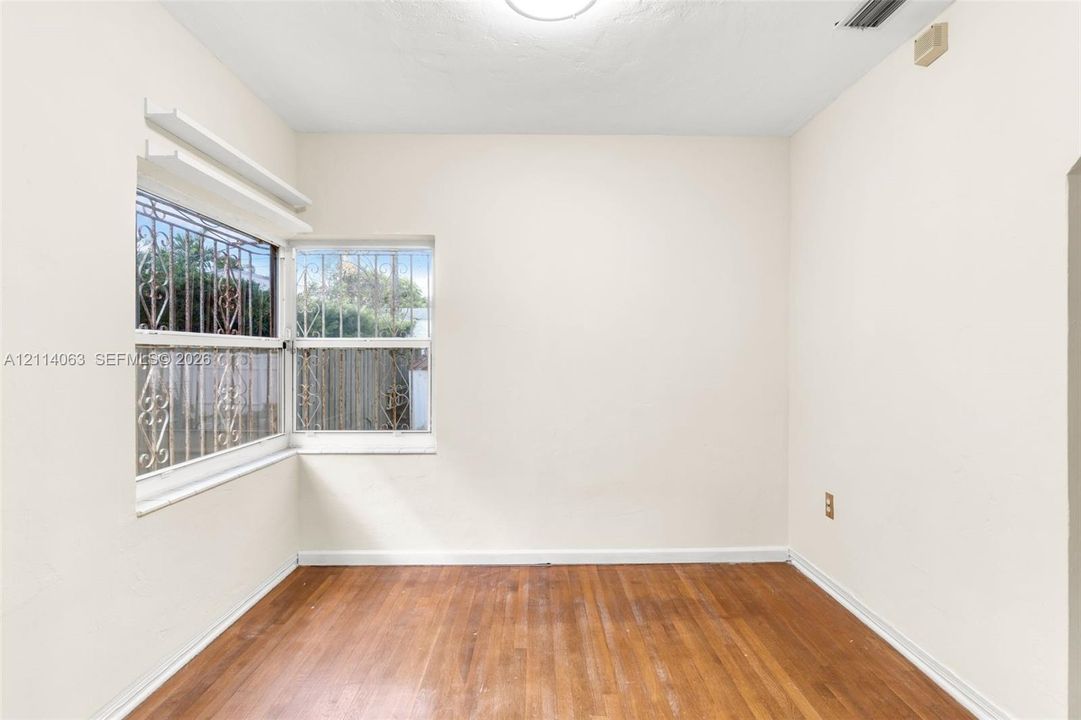 Interior room featuring wood-finish flooring, neutral wall tones, and corner windows with metal security bars