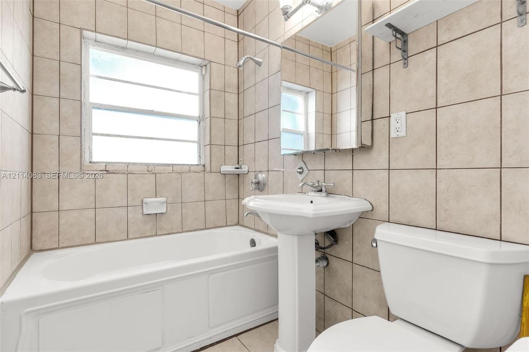 Bathroom featuring ceramic wall tiling, white porcelain pedestal sink, built-in bathtub, and integrated medicine cabinet with mirror