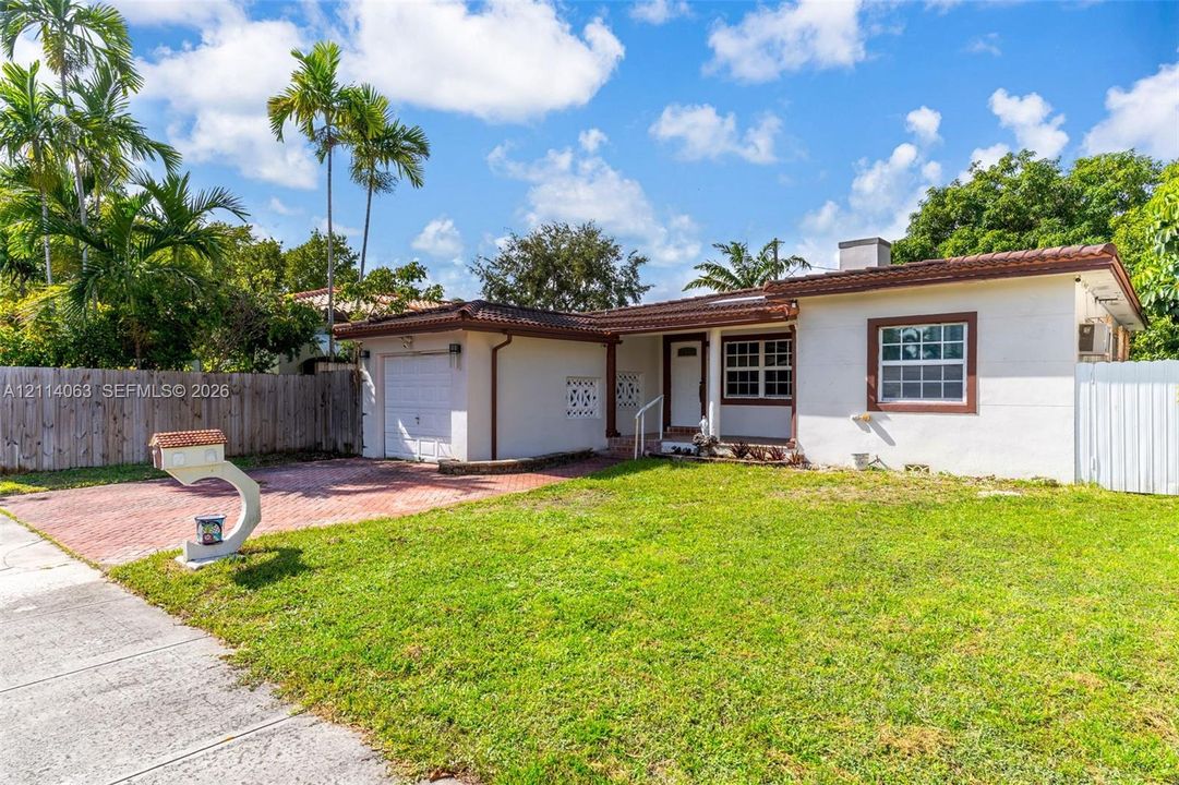 Single-story exterior featuring a tile roof, light-toned stucco facade, paved driveway, and decorative concrete masonry screen wall