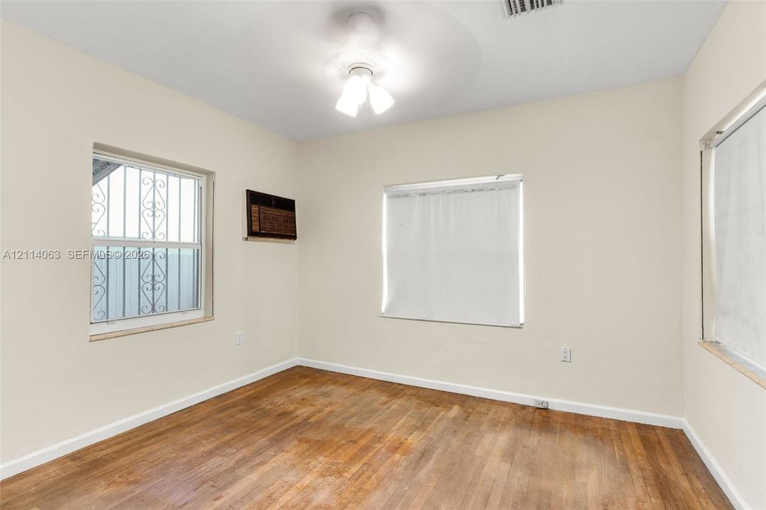 Interior room featuring wood-finish flooring, neutral wall paint, three windows, and a ceiling-mounted light fixture